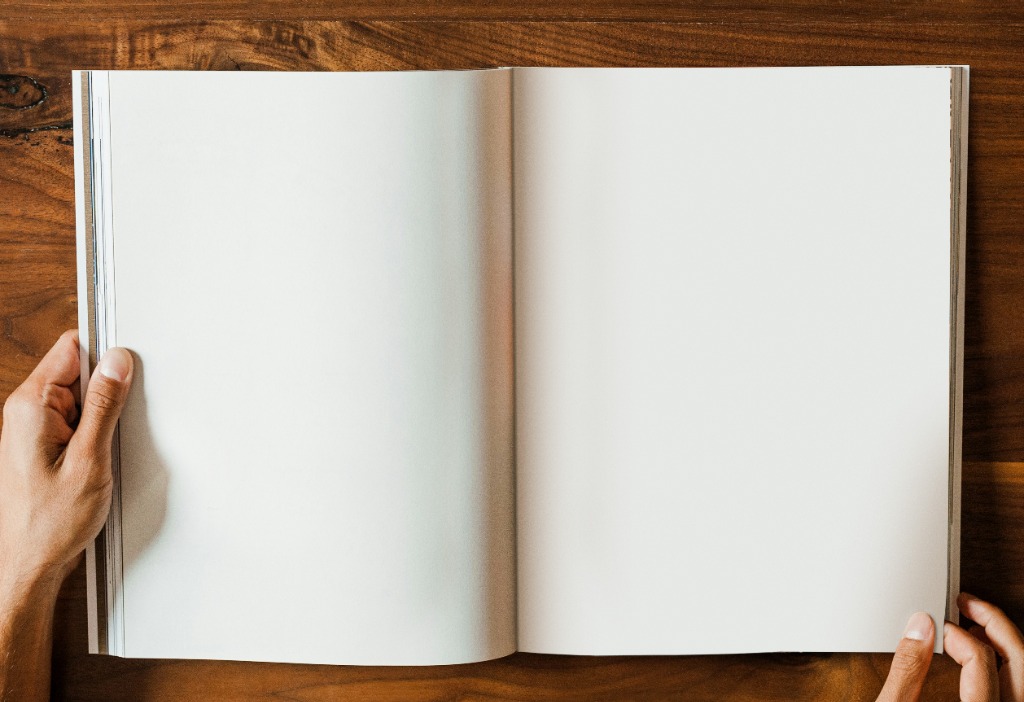 Open Magazine lying on wooden background with hands holding edges